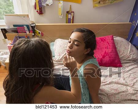 Stock Image - Mixed race girl putting lipstick on sister. Fotosearch