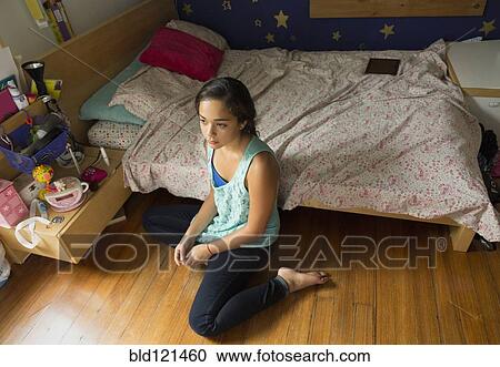 Stock Image - Mixed race girl sitting on bedroom floor. Fotosearch
