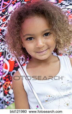 Stock Image - Mixed race girl smiling under umbrella. Fotosearch