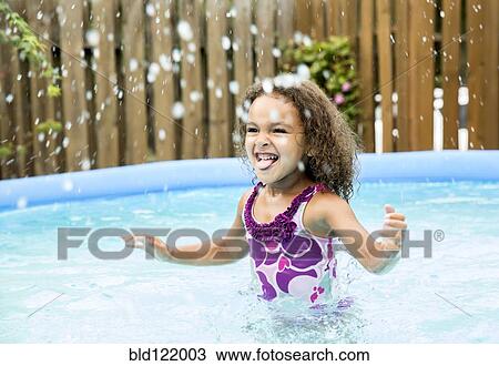 Stock Image - Mixed race girl splashing in swimming pool. Fotosearch
