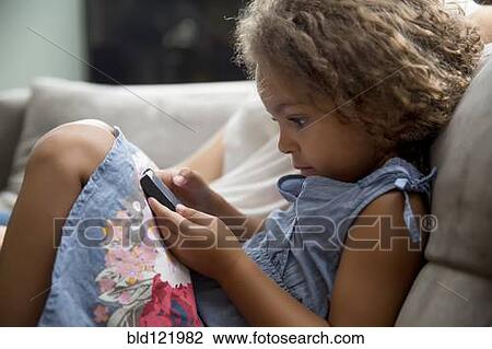 Stock Image - Mixed race girl using cell phone on sofa. Fotosearch