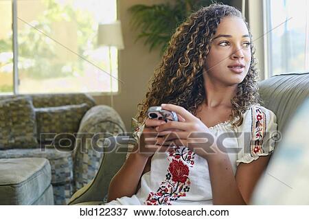 Stock Photo - Mixed race girl using cell phone on sofa. Fotosearch