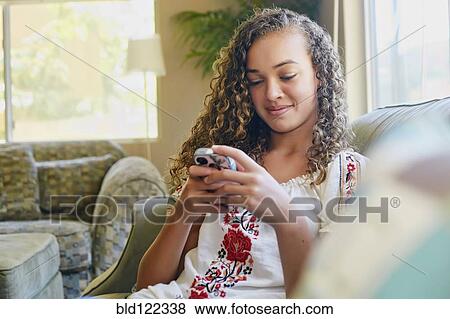 Mixed race girl using cell phone on sofa View Large Photo Image Stock Photo - Mixed race girl using cell phone on sofa. Fotosearch