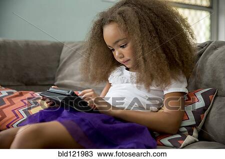 Stock Image - Mixed race girl using digital tablet on sofa. Fotosearch