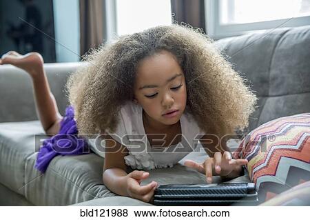 Mixed race girl using digital tablet on sofa View Large Photo Image Stock Photo - Mixed race girl using digital tablet on sofa. Fotosearch