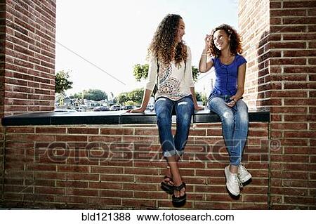 Stock Photo - Mixed race girls sitting on brick ledge. Fotosearch