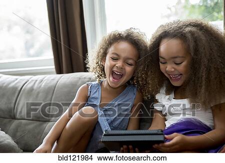 Mixed race girls using digital tablet on sofa View Large Photo Image Picture - Mixed race girls using digital tablet on sofa. Fotosearch