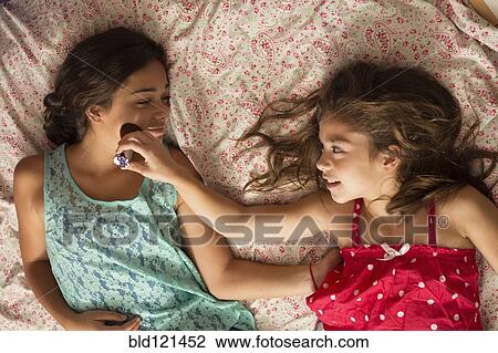 Stock Image - Mixed race sisters relaxing on bed. Fotosearch