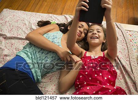 Stock Photo - Mixed race sisters using digital tablet on bed. Fotosearch