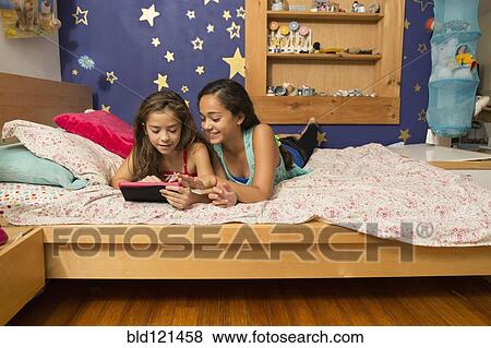Stock Photo - Mixed race sisters using digital tablet on bed. Fotosearch