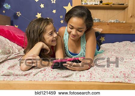 Stock Photo - Mixed race sisters using digital tablet on bed. Fotosearch