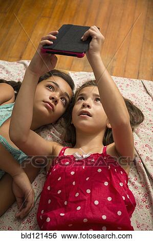 Stock Photograph - Mixed race sisters using digital tablet on bed. Fotosearch