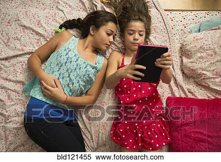 Stock Photography - Mixed race sisters using digital tablet on bed. Fotosearch