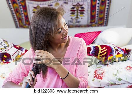 Stock Image - Mixed race teenage girl brushing hair in bedroom. Fotosearch