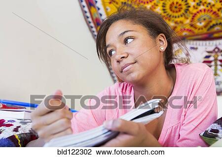 Stock Image - Mixed race teenage girl doing homework in bedroom. Fotosearch