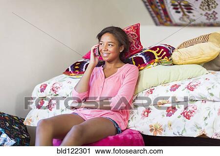 Stock Image - Mixed race teenage girl talking on cell phone in bedroom. Fotosearch