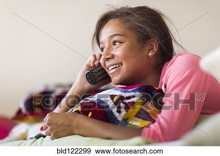 Mixed race teenage girl talking on telephone on bed View Large Photo Image Stock Photo - Mixed race teenage girl talking on telephone on bed. Fotosearch