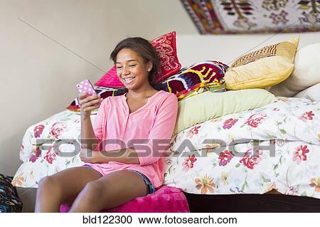 Stock Image - Mixed race teenage girl using cell phone in bedroom. Fotosearch