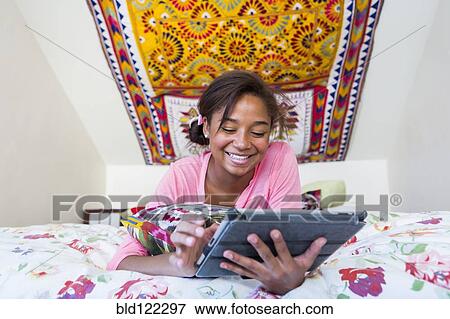 Stock Photo - Mixed race teenage girl using digital tablet on bed. Fotosearch