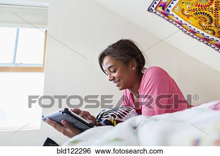 Stock Photograph - Mixed race teenage girl using digital tablet on bed. Fotosearch