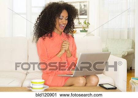 Stock Image - Mixed race woman cheering at laptop. Fotosearch