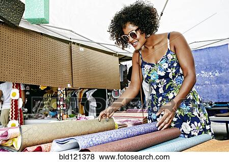 Stock Photo - Mixed race woman examining fabrics at flea market. Fotosearch