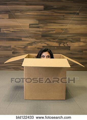 Stock Image - Mixed race woman hiding in cardboard box. Fotosearch