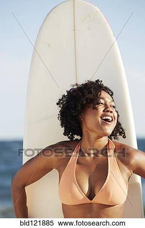 Stock Photography - Mixed race woman holding surfboard on beach. Fotosearch