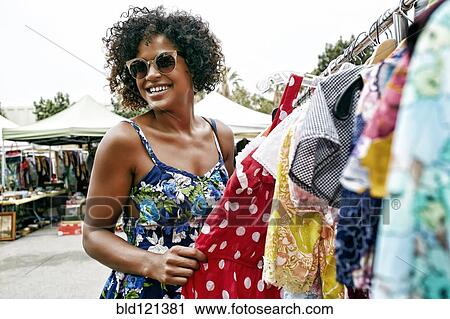Stock Image - Mixed race woman shopping at flea market. Fotosearch