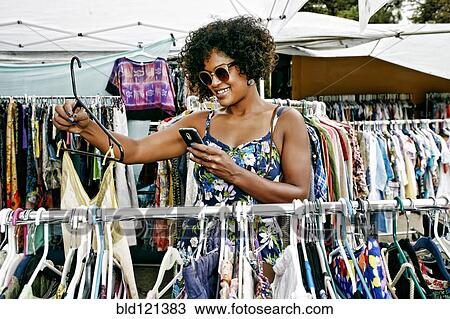 Stock Image - Mixed race woman shopping at flea market. Fotosearch
