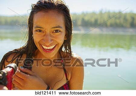 Stock Image - Mixed race woman smiling by rural lake. Fotosearch