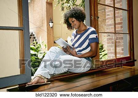 Mixed race woman using digital tablet in windowsill View Large Photo Image Stock Image - Mixed race woman using digital tablet in windowsill. Fotosearch