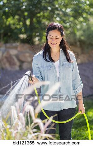 Mixed race woman watering plants in garden View Large Photo Image Stock Photography - Mixed race woman watering plants in garden. Fotosearch