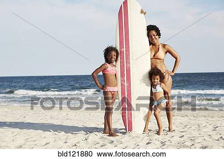 Stock Image - Mother and daughters with surfboard on beach. Fotosearch