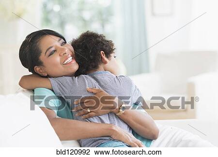Stock Image - Mother hugging son on sofa. Fotosearch