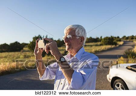 Stock Image - Senior Caucasian man taking pictures with cell phone. Fotosearch