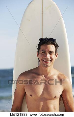 Stock Image - Smiling man with surfboard on beach. Fotosearch