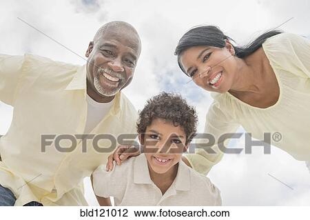 Stock Image - Three generations of family smiling in huddle outdoors. Fotosearch