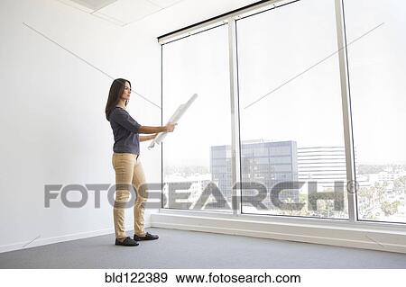 Stock Photo - Woman reading blueprints in empty office. Fotosearch