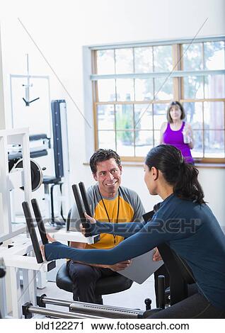 Stock Image - Woman working with personal trainer in gym. Fotosearch