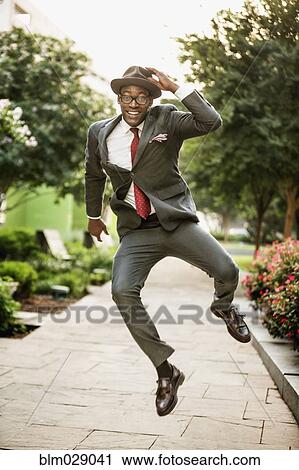 Stock Image - Black businessman skipping on city street. Fotosearch
