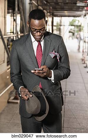 Stock Photo - Black businessman using cell phone on city street. Fotosearch