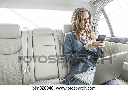 Stock Image - Businesswoman working in backseat of car. Fotosearch