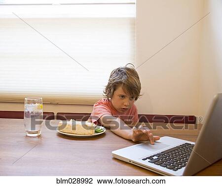 Stock Image - Caucasian boy using laptop during lunch. Fotosearch