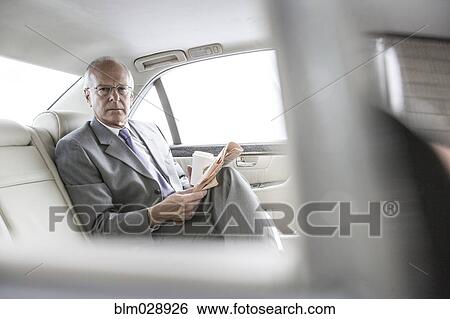 Stock Photograph - Caucasian businessman reading newspaper in car. Fotosearch