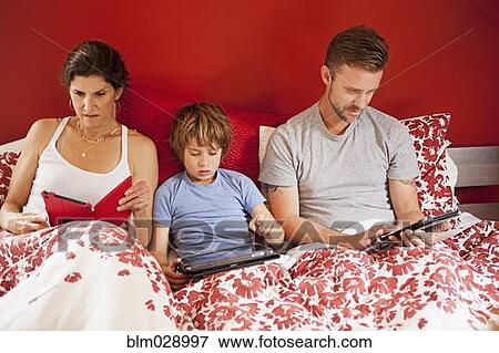 Caucasian family using digital tablets in bed View Large Photo Image Stock Photo - Caucasian family using digital tablets in bed. Fotosearch