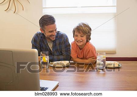 Stock Image - Caucasian father and son using laptop during lunch. Fotosearch