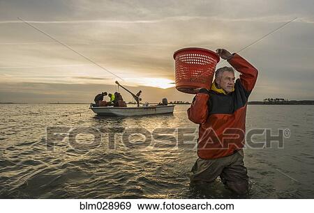 Stock Photo - Caucasian fisherman carrying basket in water. Fotosearch