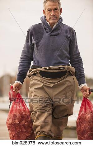 Stock Photo - Caucasian fisherman carrying catch on dock. Fotosearch