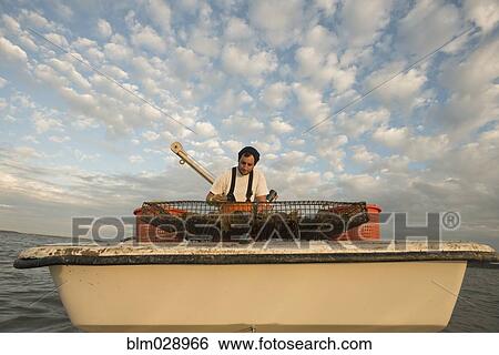Stock Photograph - Caucasian fisherman examining net on boat. Fotosearch